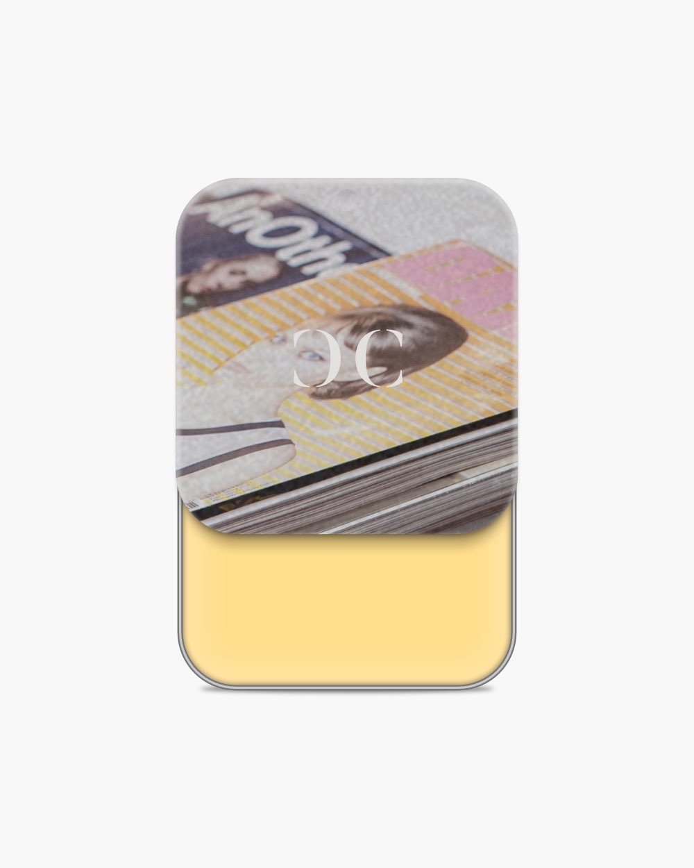 Seint Cream Corrector holding a soft butter-yellow cream beneath a lid printed with stacked fashion magazines