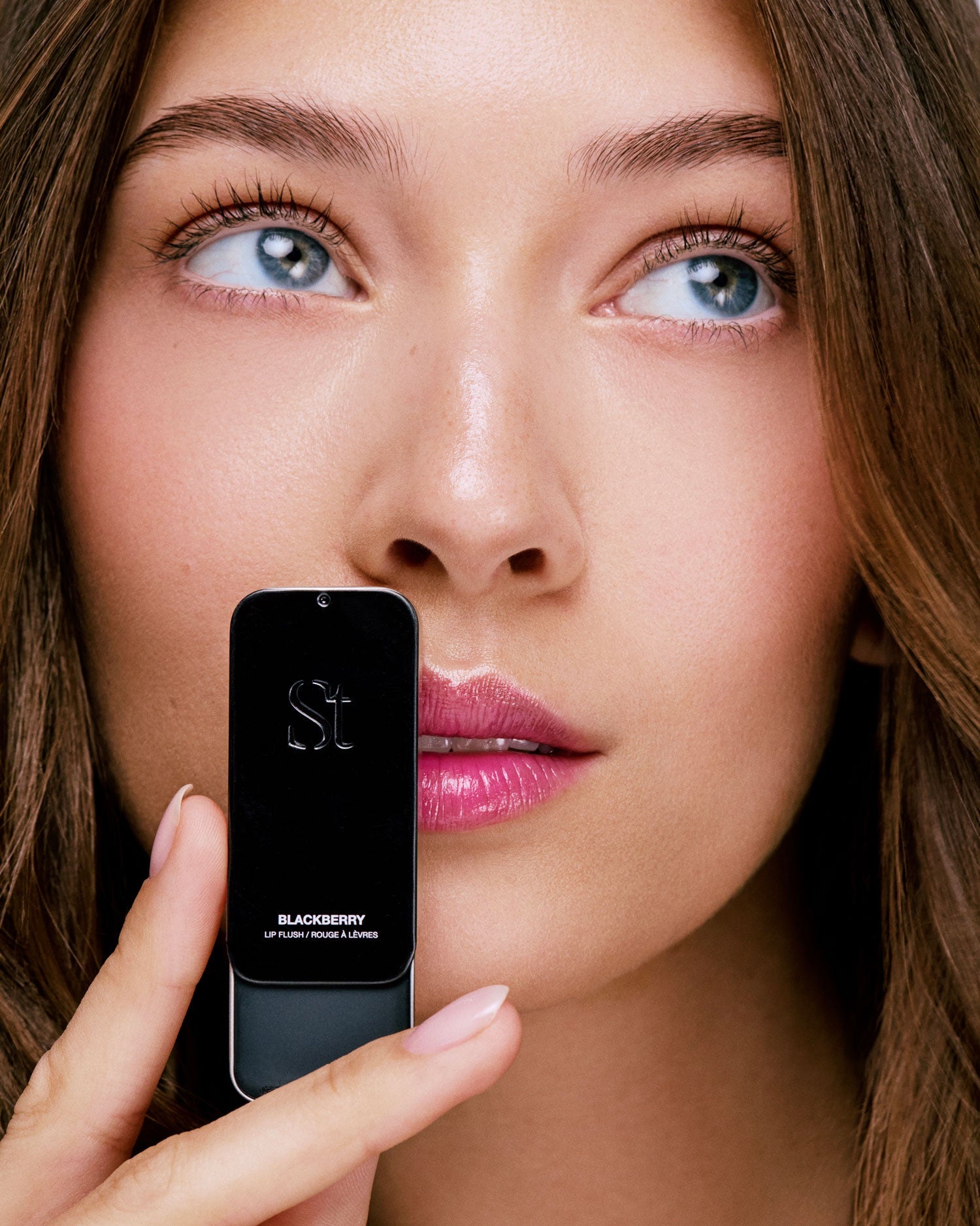 Seint Blackberry Lip Flush tin held beside a model's lips wearing the sheer berry-pink tint