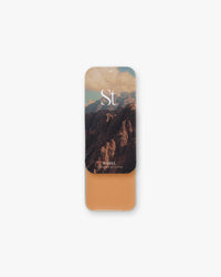 Seint Highlight in Hazel, warm russet-tan cream in a slide tin, lid showing sunset mountain cliffs