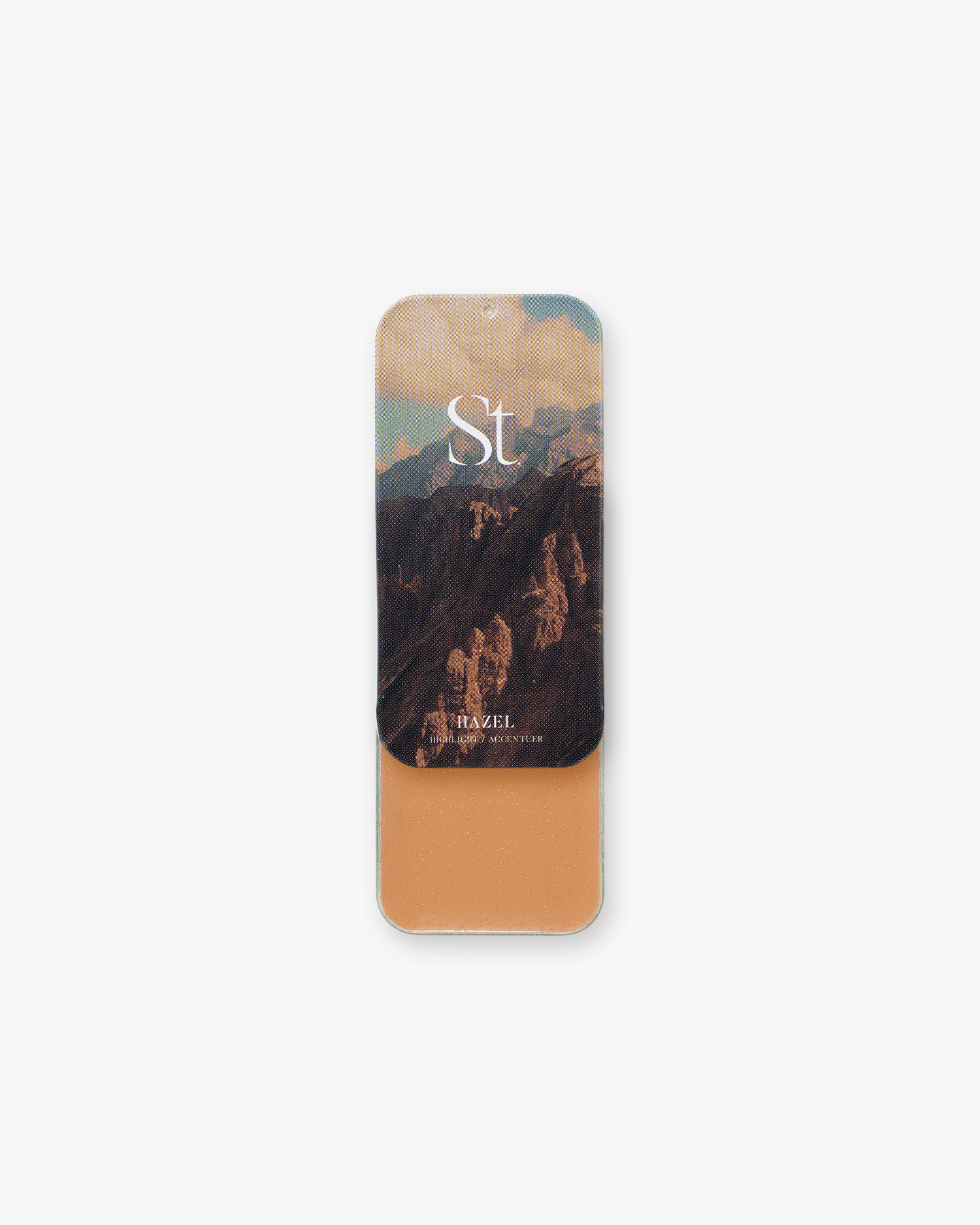 Seint Highlight in Hazel, warm russet-tan cream in a slide tin, lid showing sunset mountain cliffs