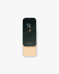Seint Highlight in Moonlit: open tin of light peachy-beige cream under a night-sky lid with a crescent moon