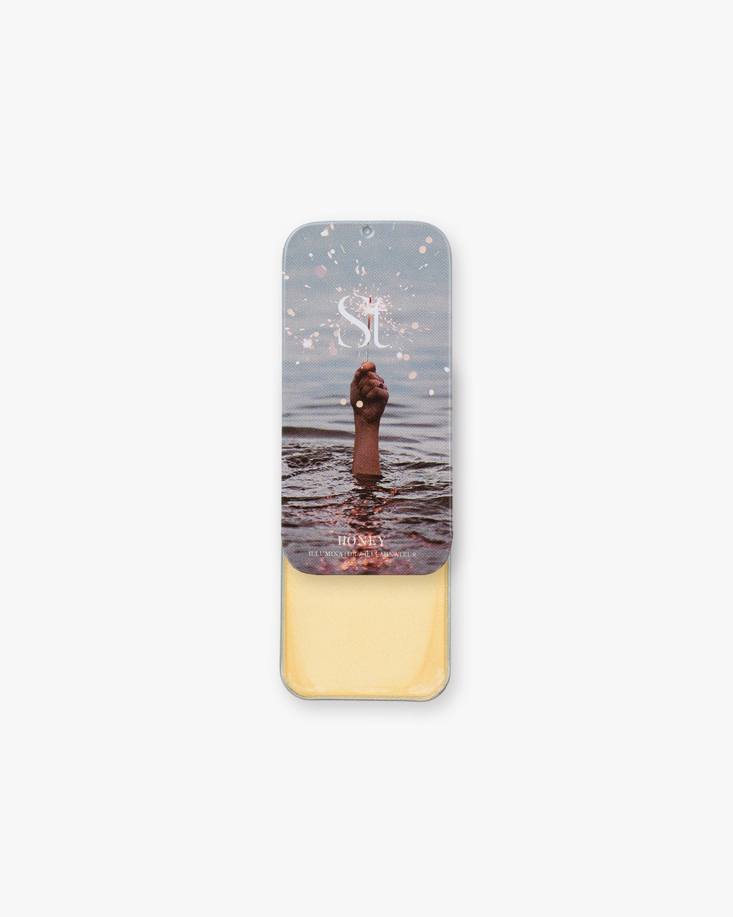Seint Illuminator in Honey slide tin, opened to pale buttery-gold cream beneath a sparkler-in-water lid photo