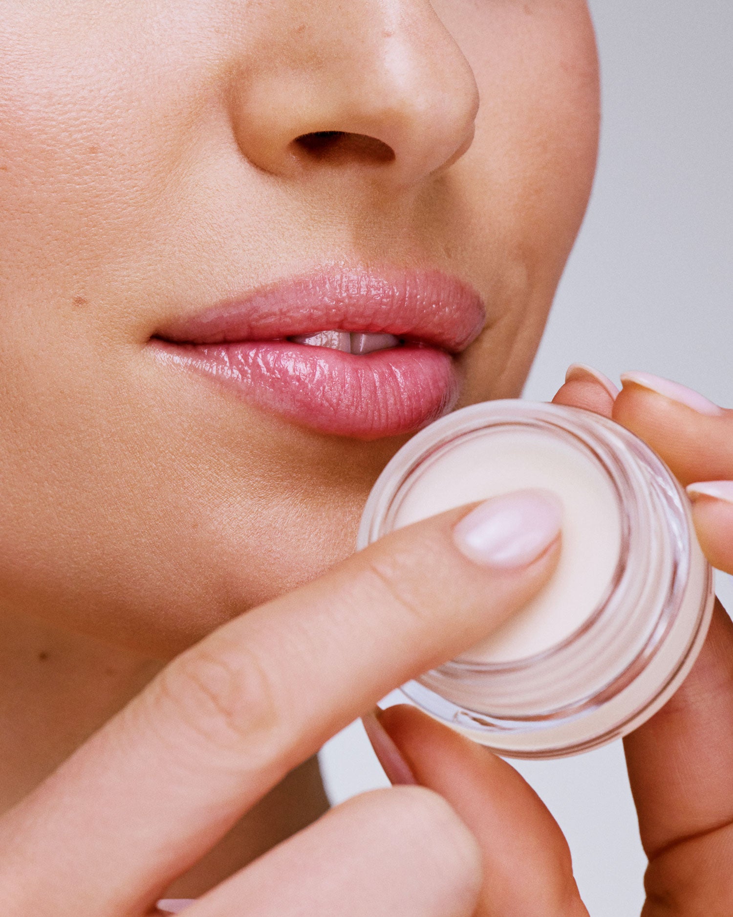 Seint Lip Balm jar held near a model's chin as she dips a fingertip into the creamy ivory balm