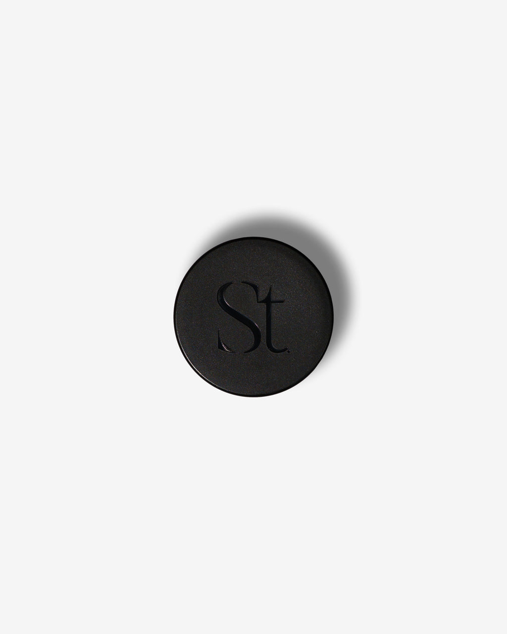Seint Lip Balm black jar lid from above, embossed with the SEINT serif wordmark