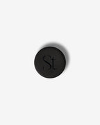Seint Lip Balm black jar lid from above, embossed with the SEINT serif wordmark