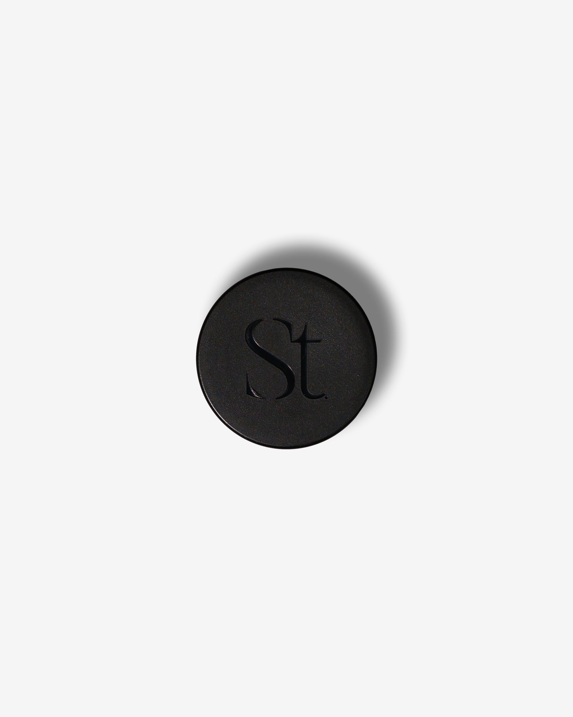 Seint Lip Balm black jar lid from above, embossed with the SEINT serif wordmark