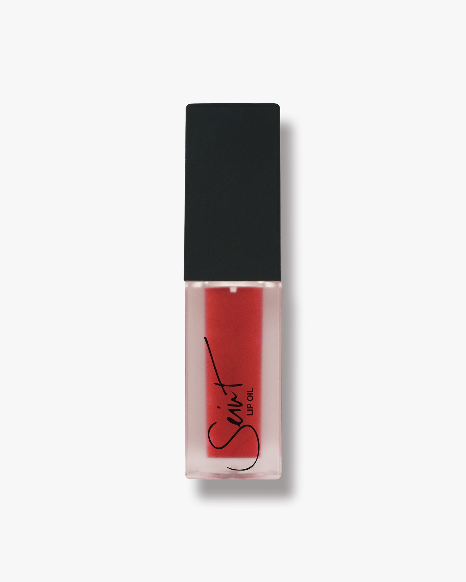 Seint Lip Oil in Caramel Apple, a bright cherry-red tint in a frosted bottle with matte black cap
