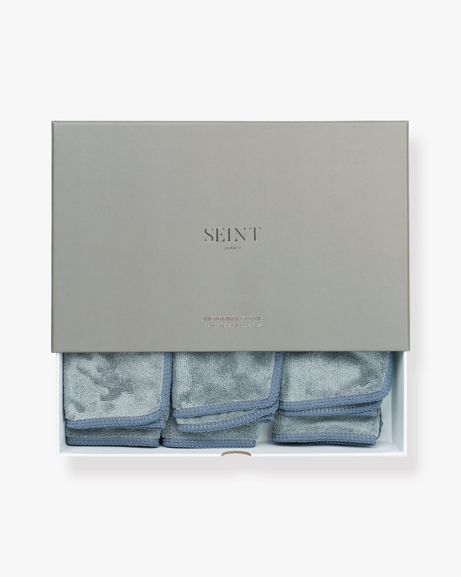 Seint Microfiber Cloths — grey box lifted to reveal three folded grey-blue cloths with stitched edges
