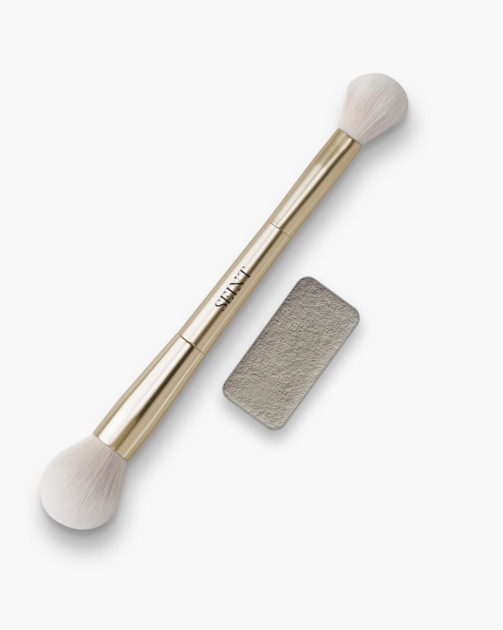 Seint Powder Bundle pairing a gold double-ended brush with a pan of finely textured, pale gray-beige Feather Blotting Dust