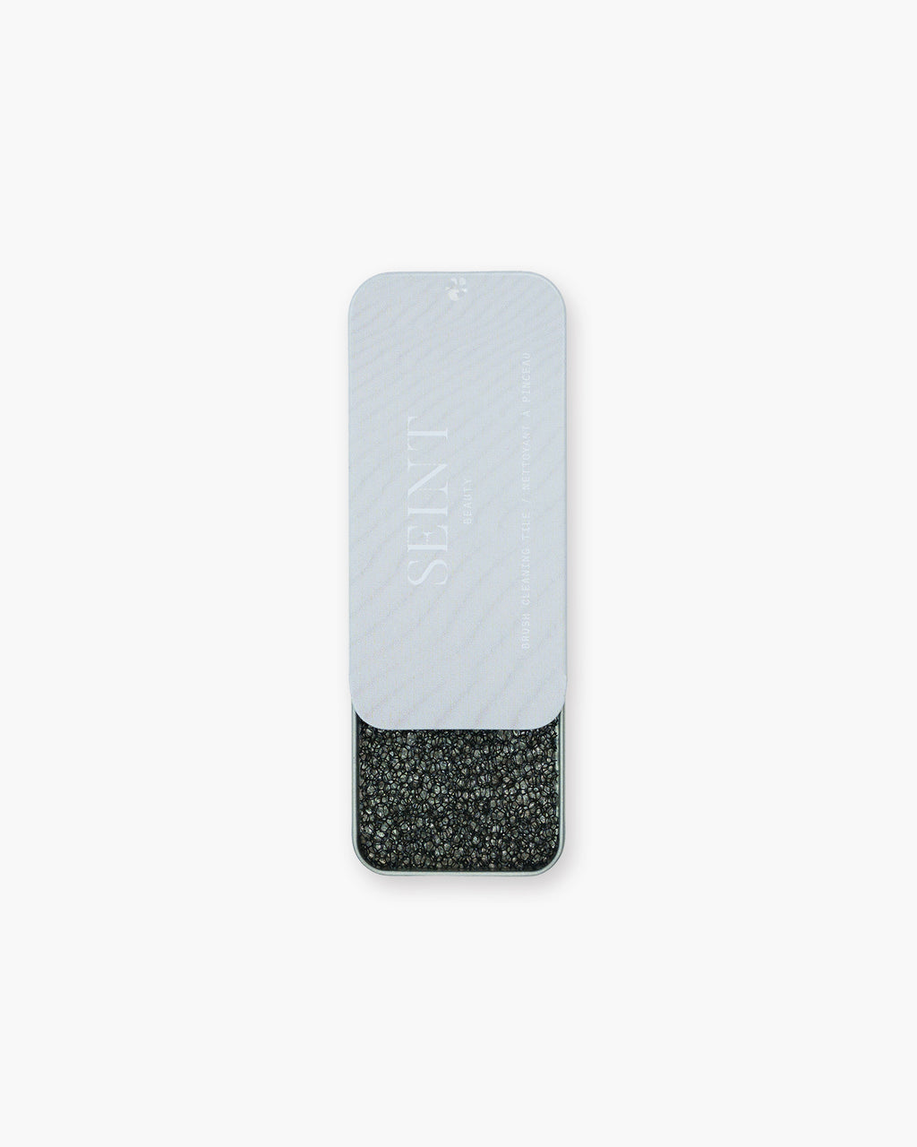 Seint Brush Cleaning Tile tin slid open beneath its pale gray Seint Beauty lid, revealing the charcoal textured tile