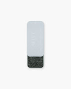 Seint Brush Cleaning Tile tin slid open beneath its pale gray Seint Beauty lid, revealing the charcoal textured tile
