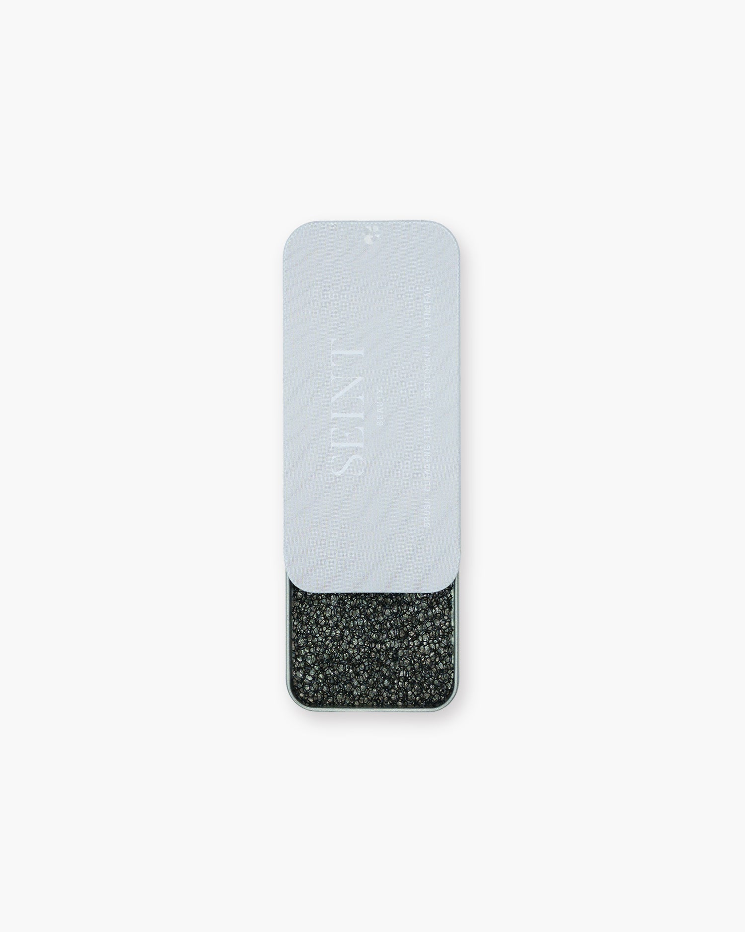 Seint Brush Cleaning Tile tin slid open beneath its pale gray Seint Beauty lid, revealing the charcoal textured tile