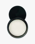 Seint Brush Cleansing Soap opened to show a white soap bar, with the tin's dotted black silicone scrubbing pad behind