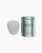 Seint Perfector blending sponge in soft gray beside its closed silver storage tin with Seint Beauty label