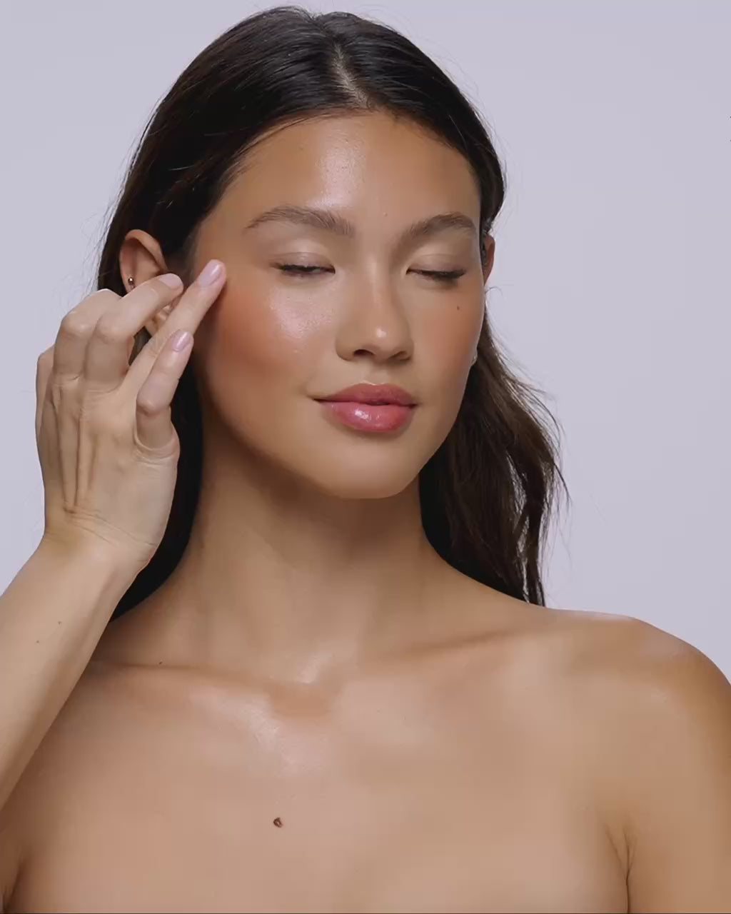 Video: model smooths Seint Illuminator onto her cheekbone with fingertips for a dewy glow