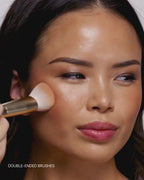 Video: model blends cream makeup on her cheek with a double-ended gold Seint brush