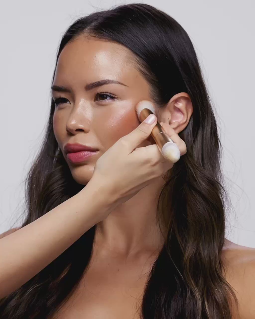 Video: model applies Seint Bronzer to her cheekbone with a double-ended gold brush