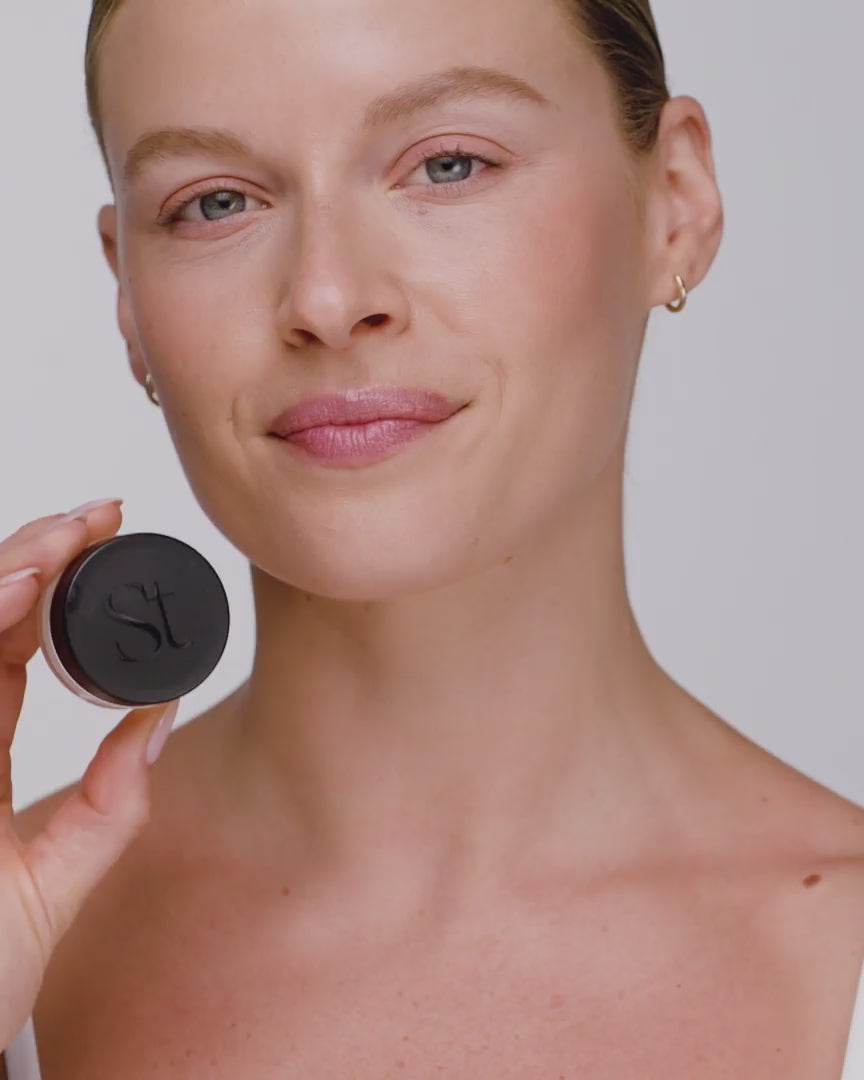 Video: smiling model holds the closed Seint Lip Balm jar beside her jaw to show the black lid