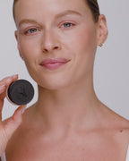 Video: smiling model holds the closed Seint Lip Balm jar beside her jaw to show the black lid