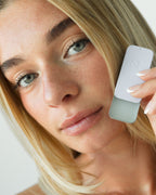 Seint Saved Salve open tin held up by a model with soft glossy lips, her face tilted toward the camera